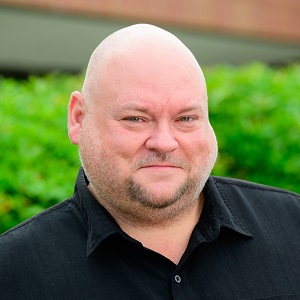 Keith, a white man with no hair and small gray chin beard. He smiles while outside, wearing a black shirt.