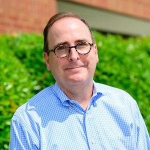 Kevin, a white man with cropped brown hair and glasses wearing a blue collared shirt while smiling outside.