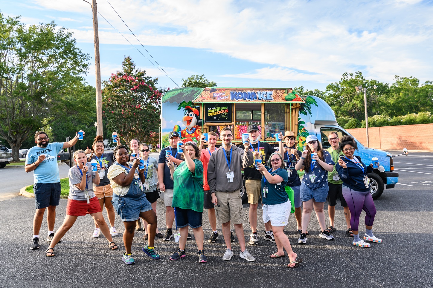 Diverse youth with disabilities and staff pose with frozen ice treats by a food truck outside.