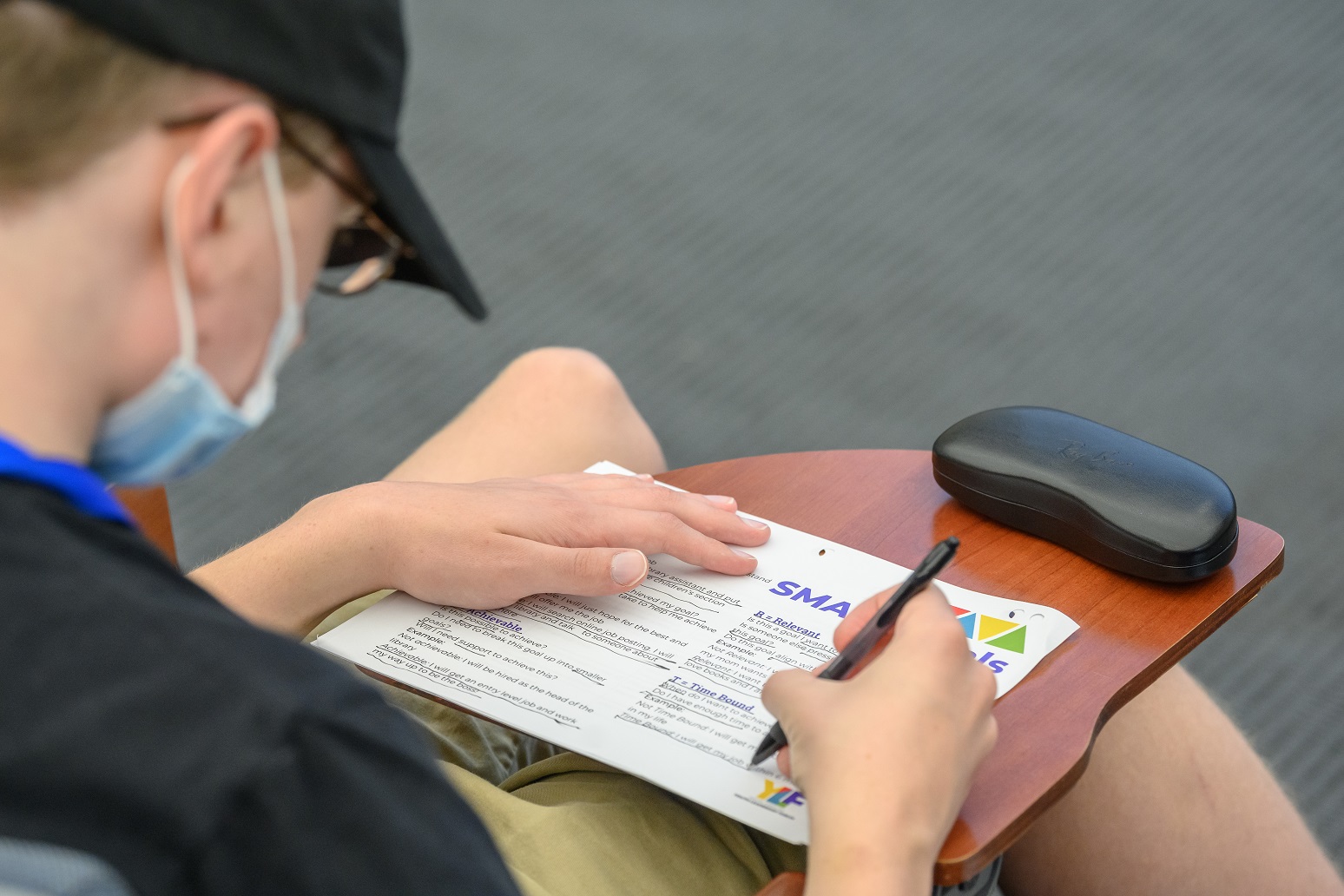 Young white disabled student wearing a facemask working on a 'Smart Goals' worksheet.