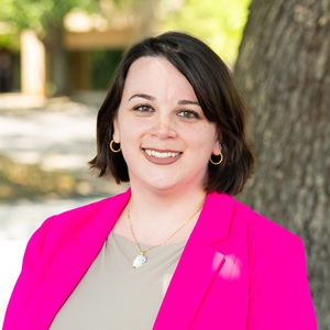 Renata, a white woman with short brown hair smiling in a pink blazer while outside.
