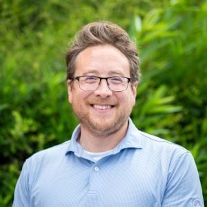 Matt, a white man with glasses smiling outside.