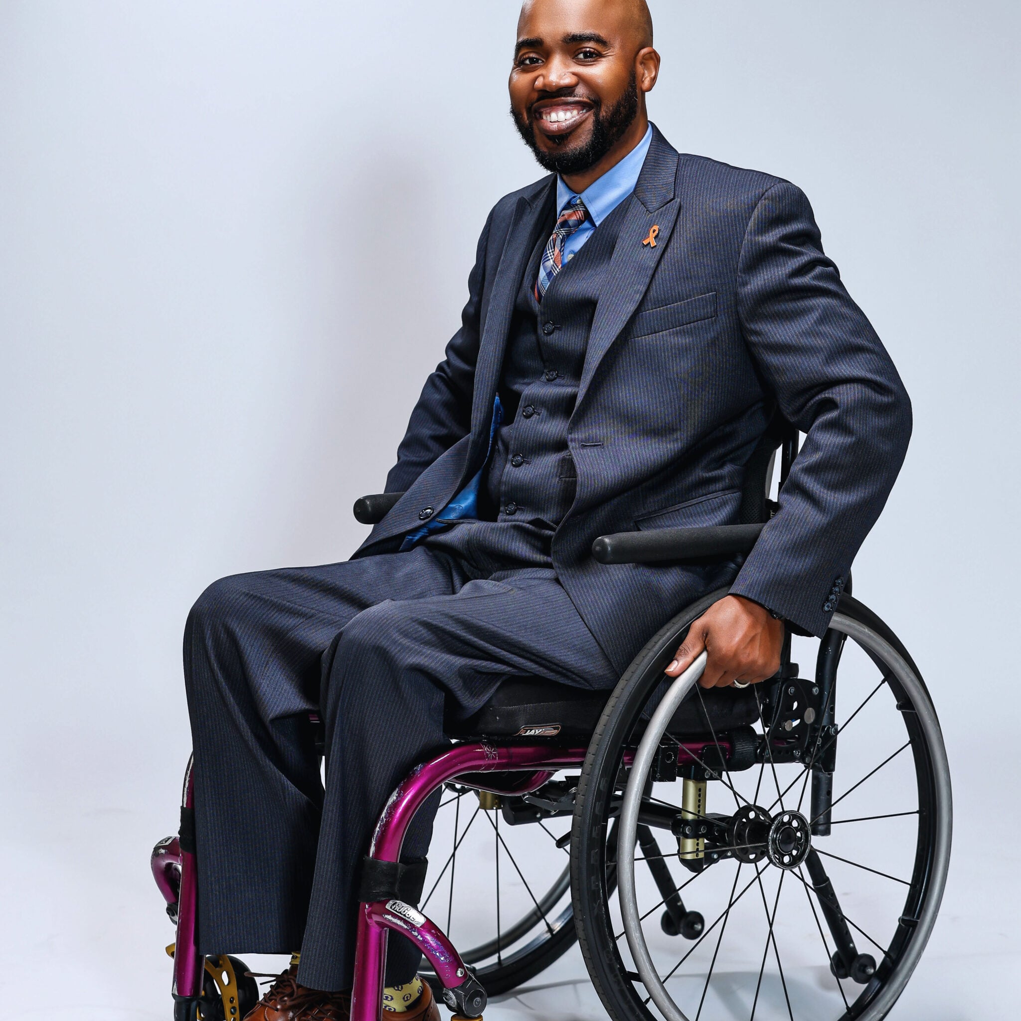 Corey, A Black man in a suit using a wheelchair.